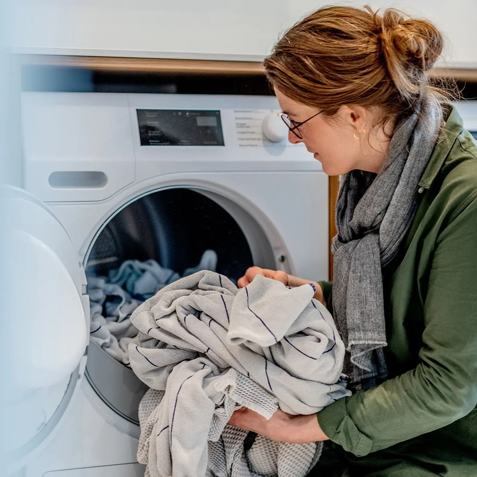 Kvinde der putter tøj i vaskemaskine. El for privatforbrugere